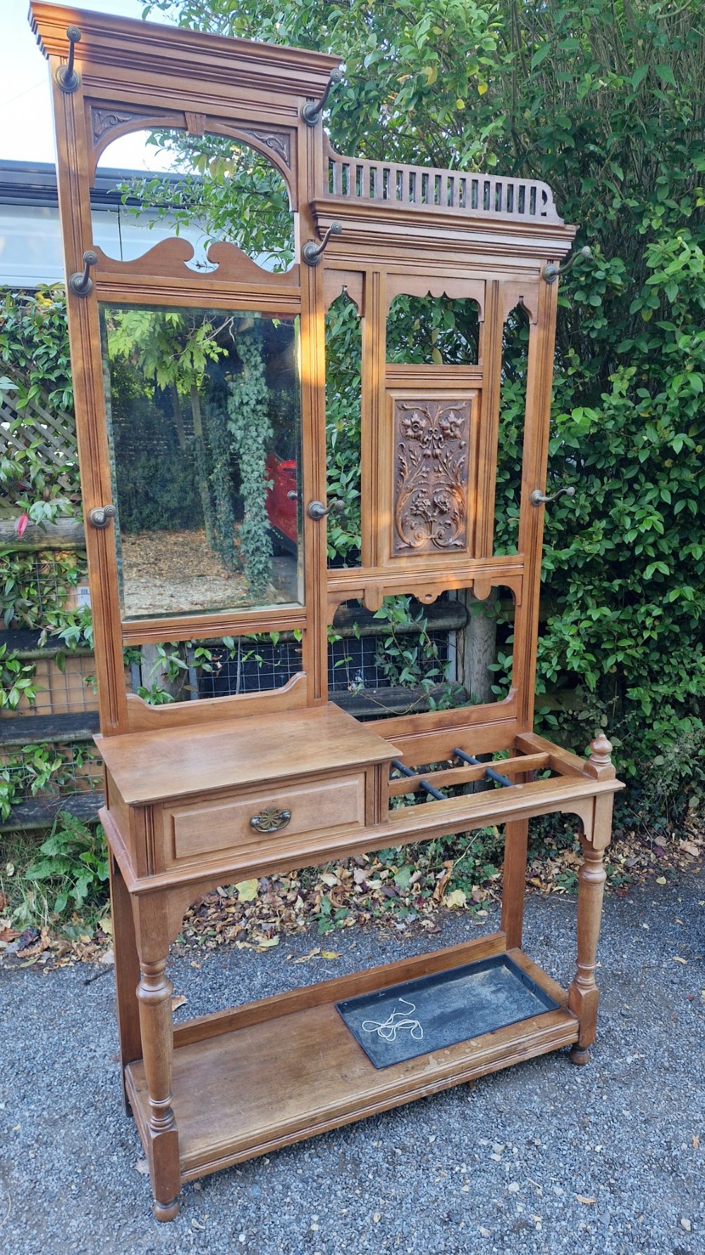 A late Victorian walnut hall stand featuring a central rectangular mirror, carved floral wood panel, brass hooks, a glove drawer, and an umbrella rack with drip tray.