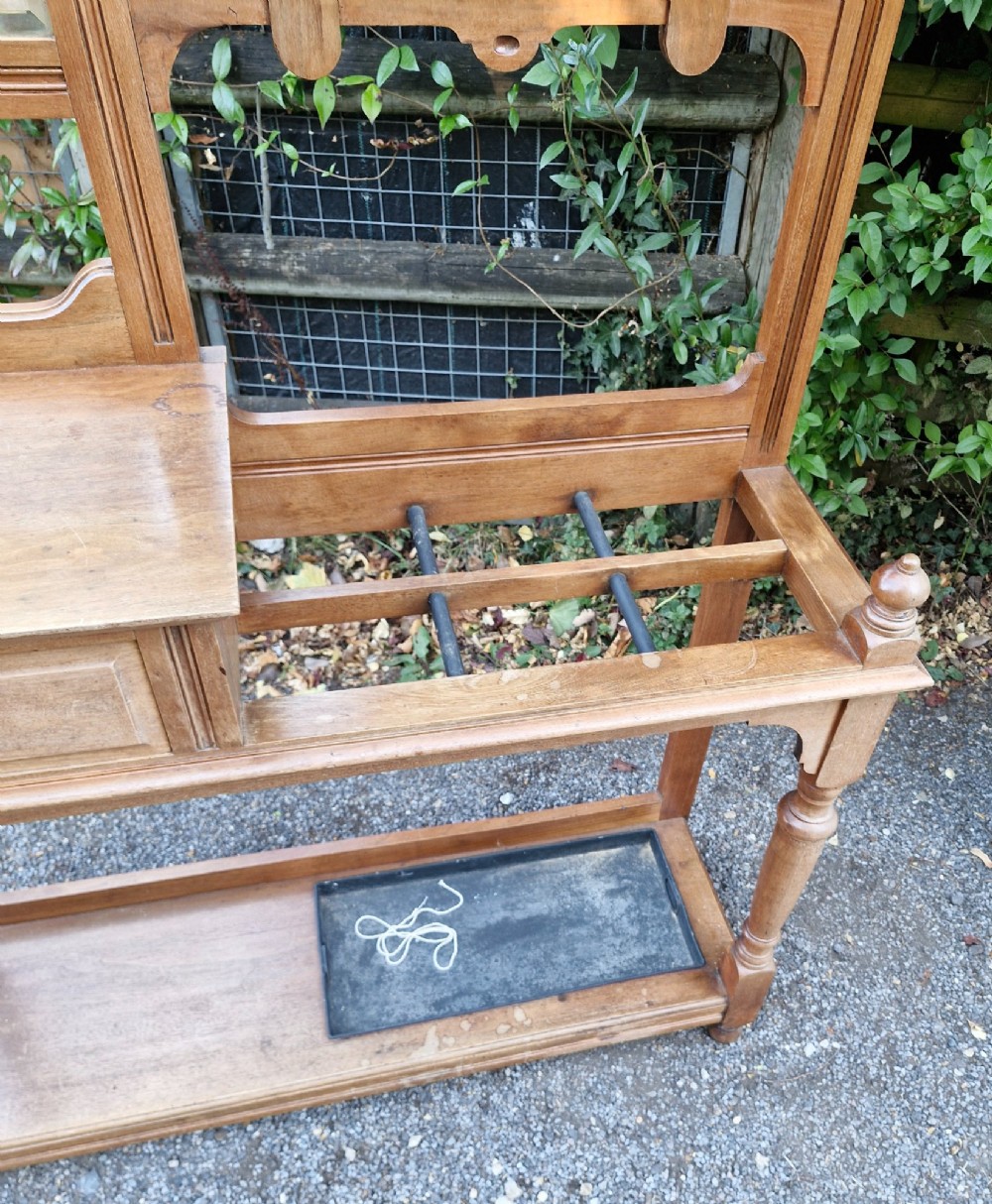 A late Victorian walnut hall stand featuring a central rectangular mirror, carved floral wood panel, brass hooks, a glove drawer, and an umbrella rack with drip tray. View II