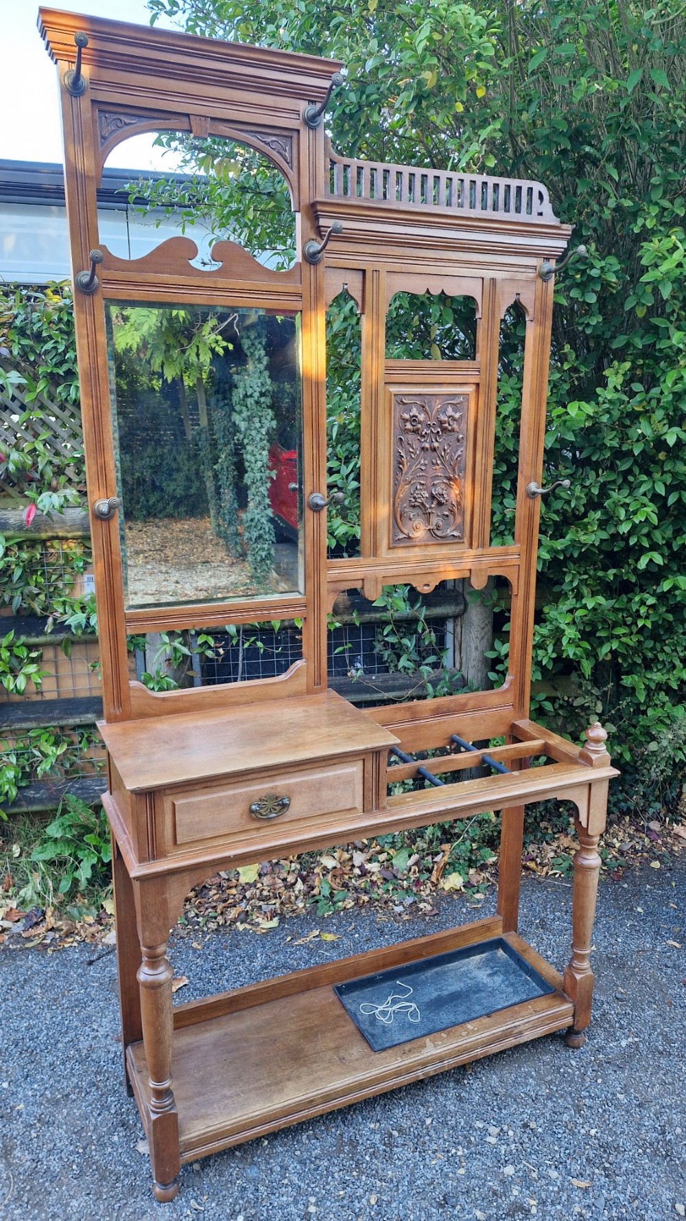 A late Victorian walnut hall stand featuring a central rectangular mirror, carved floral wood panel, brass hooks, a glove drawer, and an umbrella rack with drip tray. View III