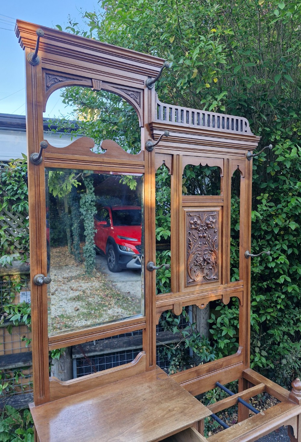 A late Victorian walnut hall stand featuring a central rectangular mirror, carved floral wood panel, brass hooks, a glove drawer, and an umbrella rack with drip tray. View IV