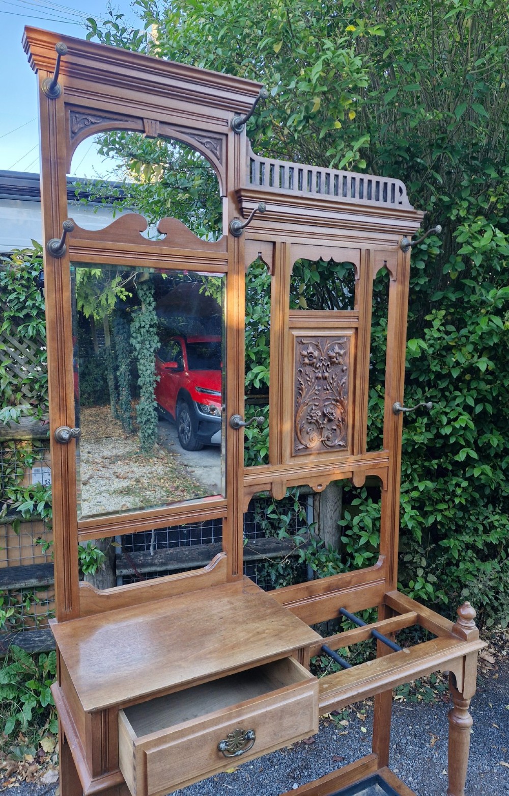 A late Victorian walnut hall stand featuring a central rectangular mirror, carved floral wood panel, brass hooks, a glove drawer, and an umbrella rack with drip tray. View V