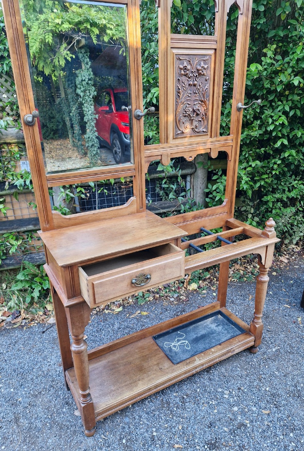 A late Victorian walnut hall stand featuring a central rectangular mirror, carved floral wood panel, brass hooks, a glove drawer, and an umbrella rack with drip tray. View VI