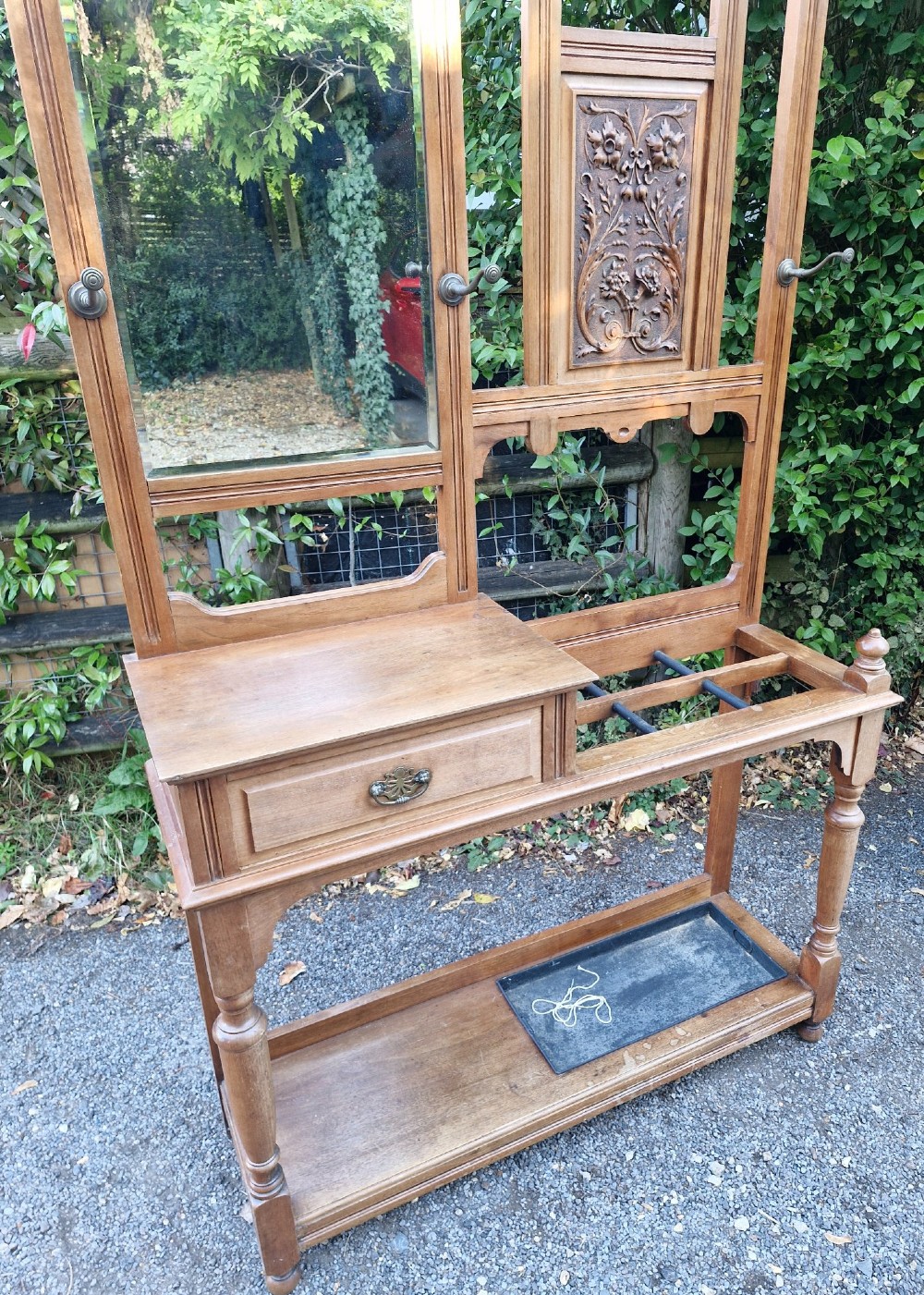 A late Victorian walnut hall stand featuring a central rectangular mirror, carved floral wood panel, brass hooks, a glove drawer, and an umbrella rack with drip tray. View VII