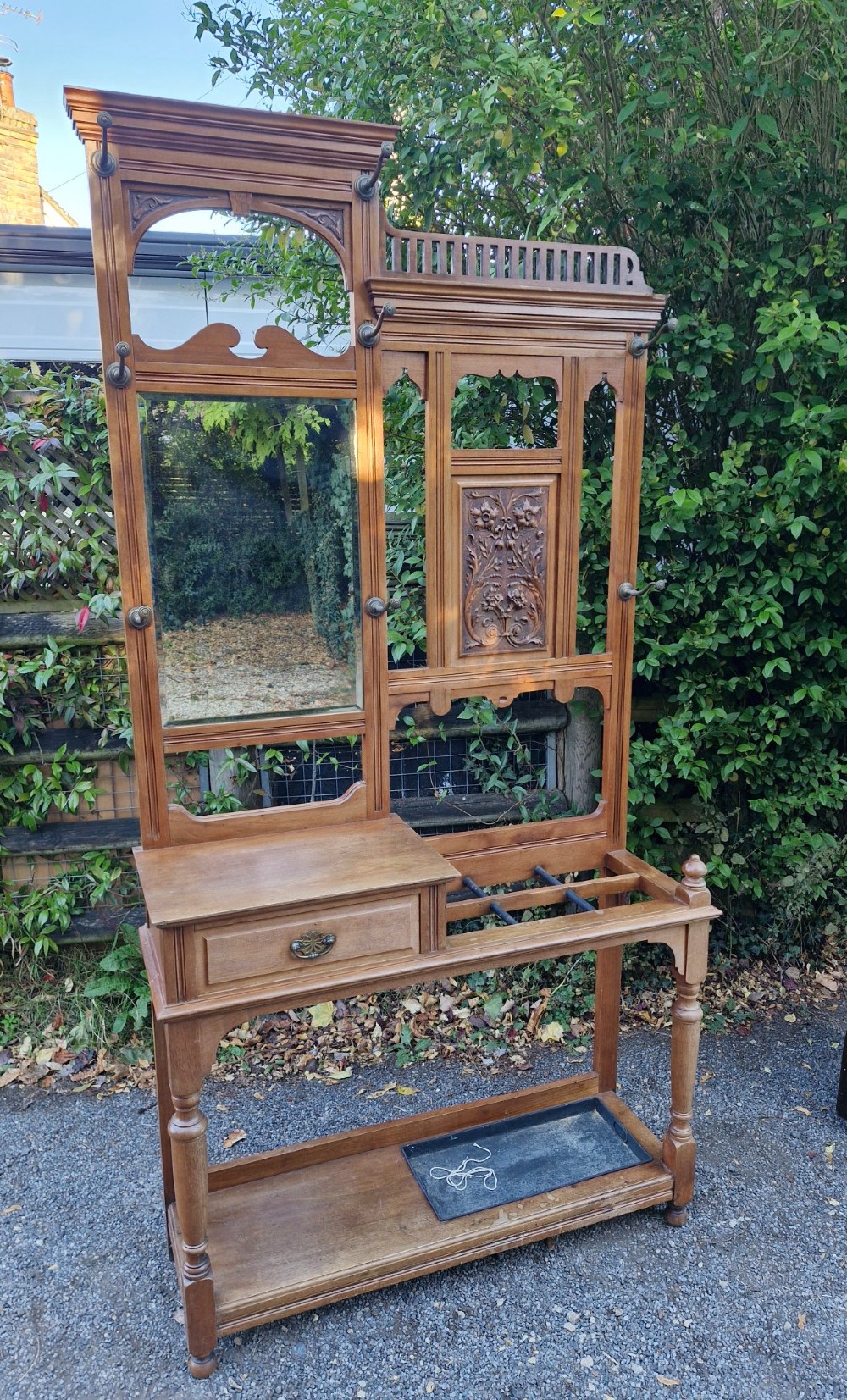 A late Victorian walnut hall stand featuring a central rectangular mirror, carved floral wood panel, brass hooks, a glove drawer, and an umbrella rack with drip tray. View VIII