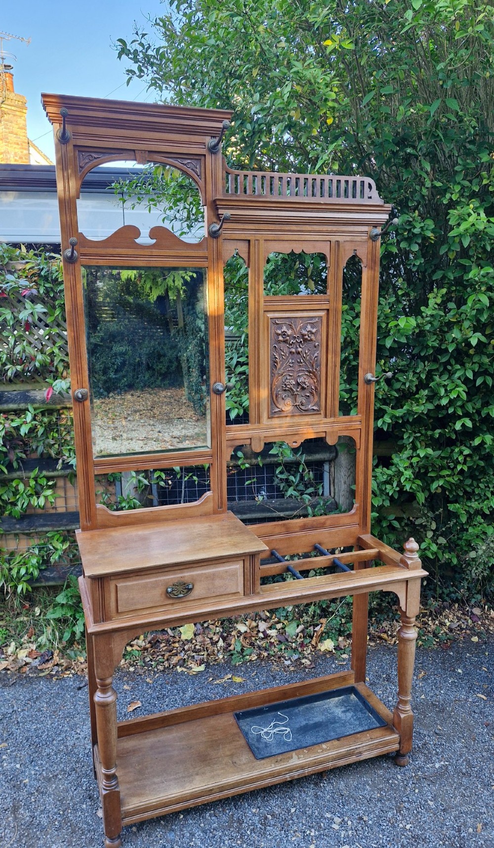 A late Victorian walnut hall stand featuring a central rectangular mirror, carved floral wood panel, brass hooks, a glove drawer, and an umbrella rack with drip tray. View IX
