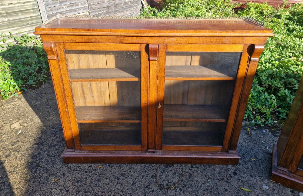 A pair of Victorian low oak bookcases featuring glazed twin doors, brass top gallery rails, carved corbels, and adjustable interior shelving. View II
