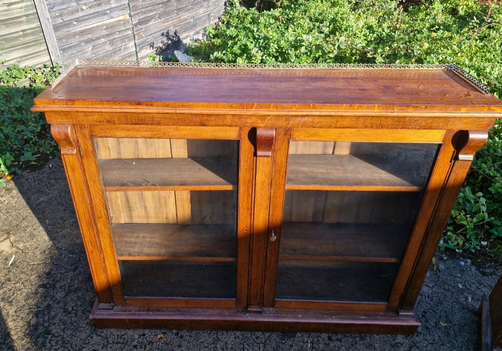A pair of Victorian low oak bookcases featuring glazed twin doors, brass top gallery rails, carved corbels, and adjustable interior shelving. View III