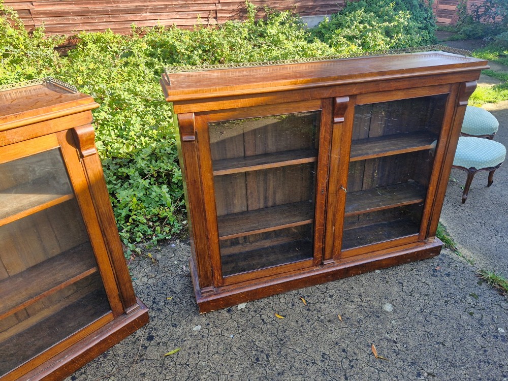 A pair of Victorian low oak bookcases featuring glazed twin doors, brass top gallery rails, carved corbels, and adjustable interior shelving. View IV