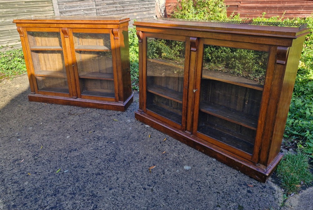 A pair of Victorian low oak bookcases featuring glazed twin doors, brass top gallery rails, carved corbels, and adjustable interior shelving. View V