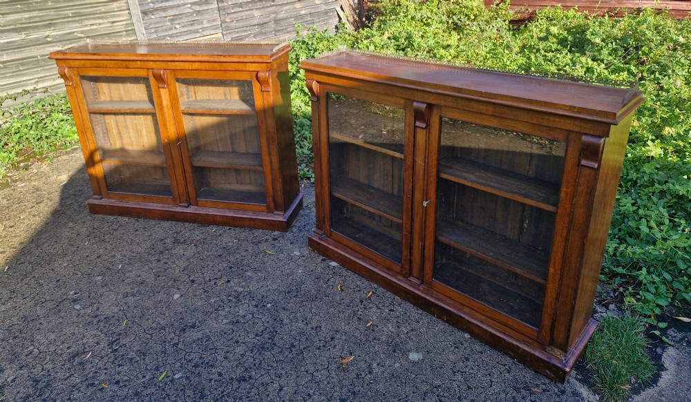 A pair of Victorian low oak bookcases featuring glazed twin doors, brass top gallery rails, carved corbels, and adjustable interior shelving. View VI
