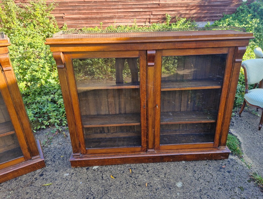 A pair of Victorian low oak bookcases featuring glazed twin doors, brass top gallery rails, carved corbels, and adjustable interior shelving. View VII