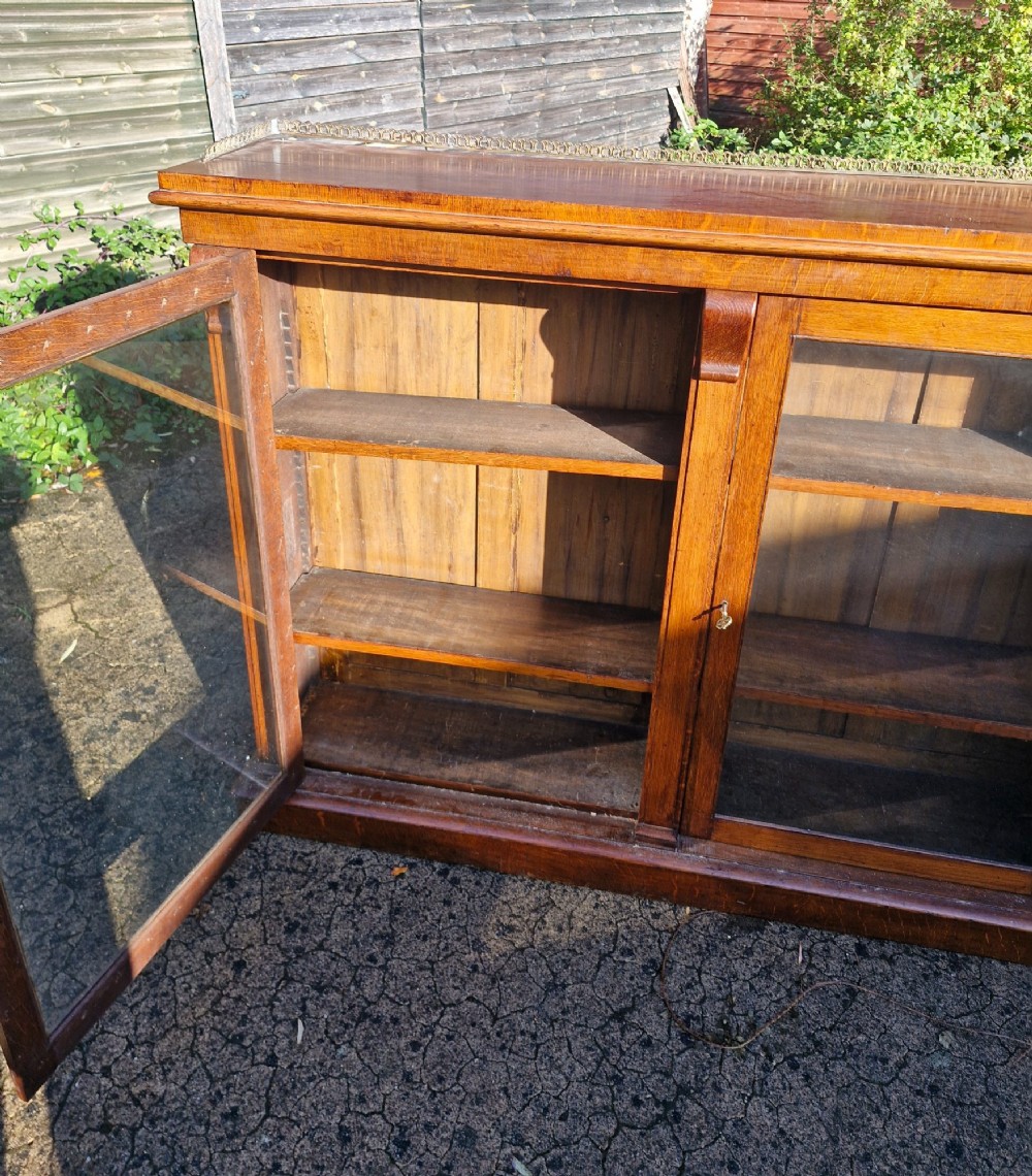 A pair of Victorian low oak bookcases featuring glazed twin doors, brass top gallery rails, carved corbels, and adjustable interior shelving. View IX