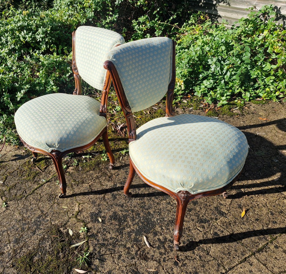 A pair of late Victorian walnut frame bedroom chairs with light green patterned upholstery and carved cabriole legs on brass castors.