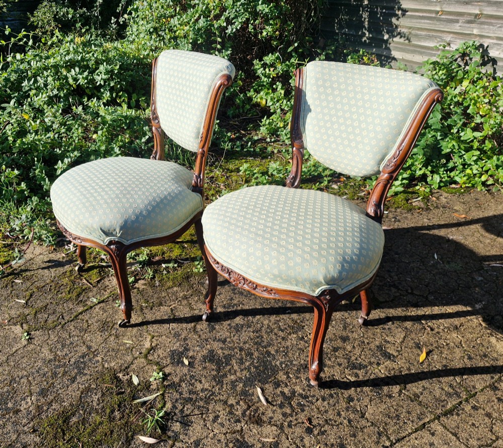 A pair of late Victorian walnut frame bedroom chairs with light green patterned upholstery and carved cabriole legs on brass castors. View II