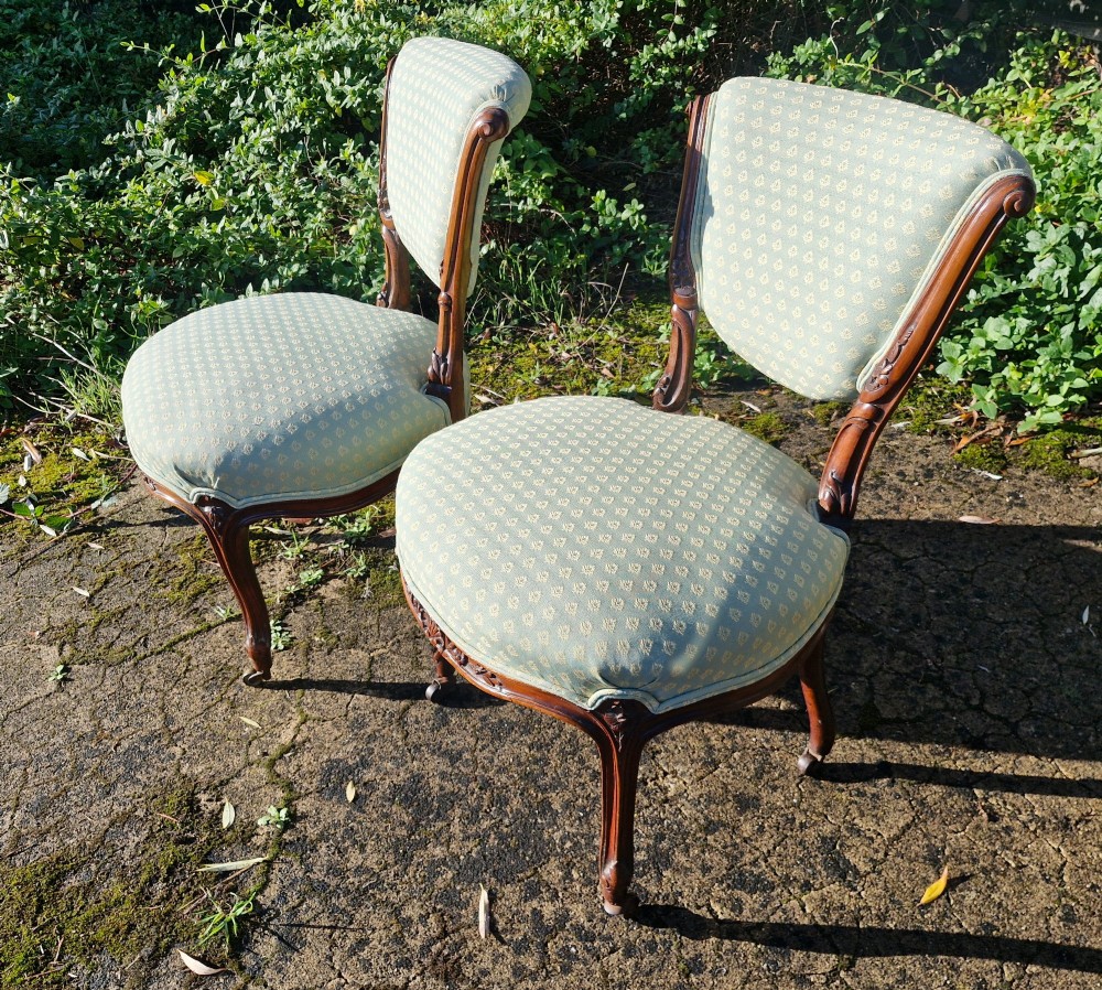 A pair of late Victorian walnut frame bedroom chairs with light green patterned upholstery and carved cabriole legs on brass castors. View V
