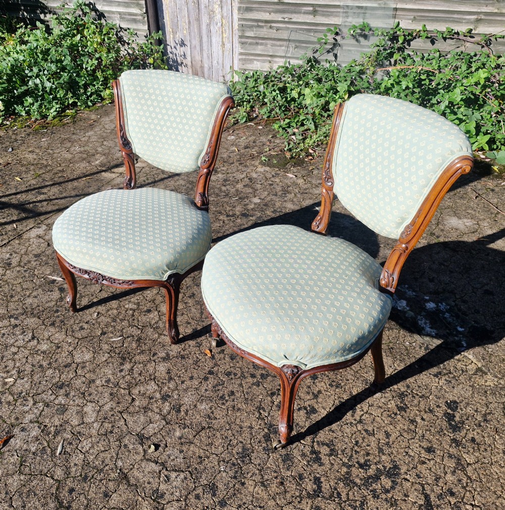 A pair of late Victorian low-seated bedroom chairs with carved walnut frames and light green patterned upholstery.