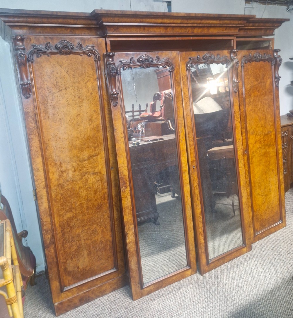 A large Victorian breakfront wardrobe crafted from highly figured burr walnut with two central mirrored doors and carved scrollwork details.