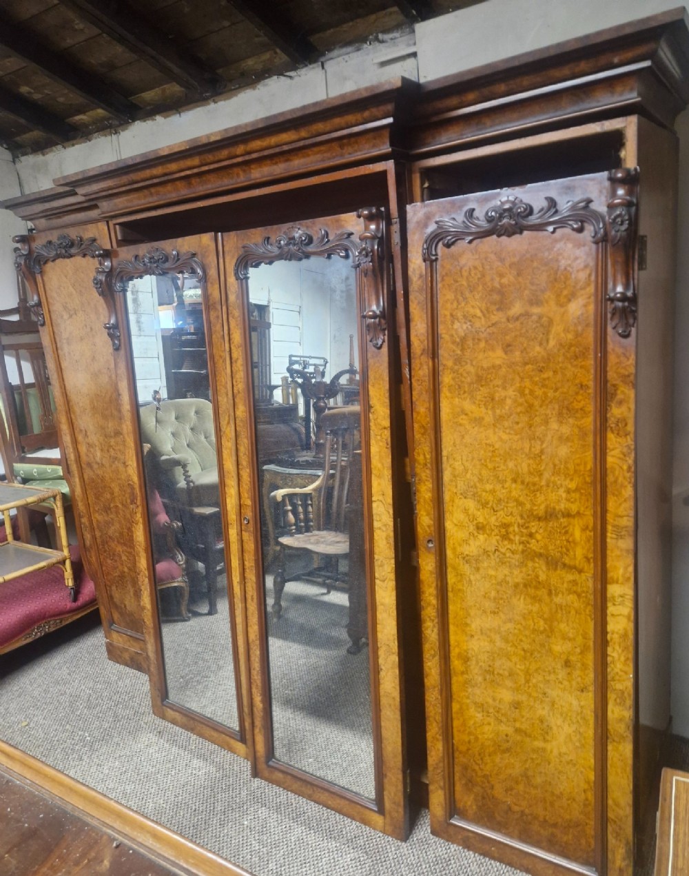 A large Victorian breakfront wardrobe crafted from highly figured burr walnut with two central mirrored doors and carved scrollwork details. View III