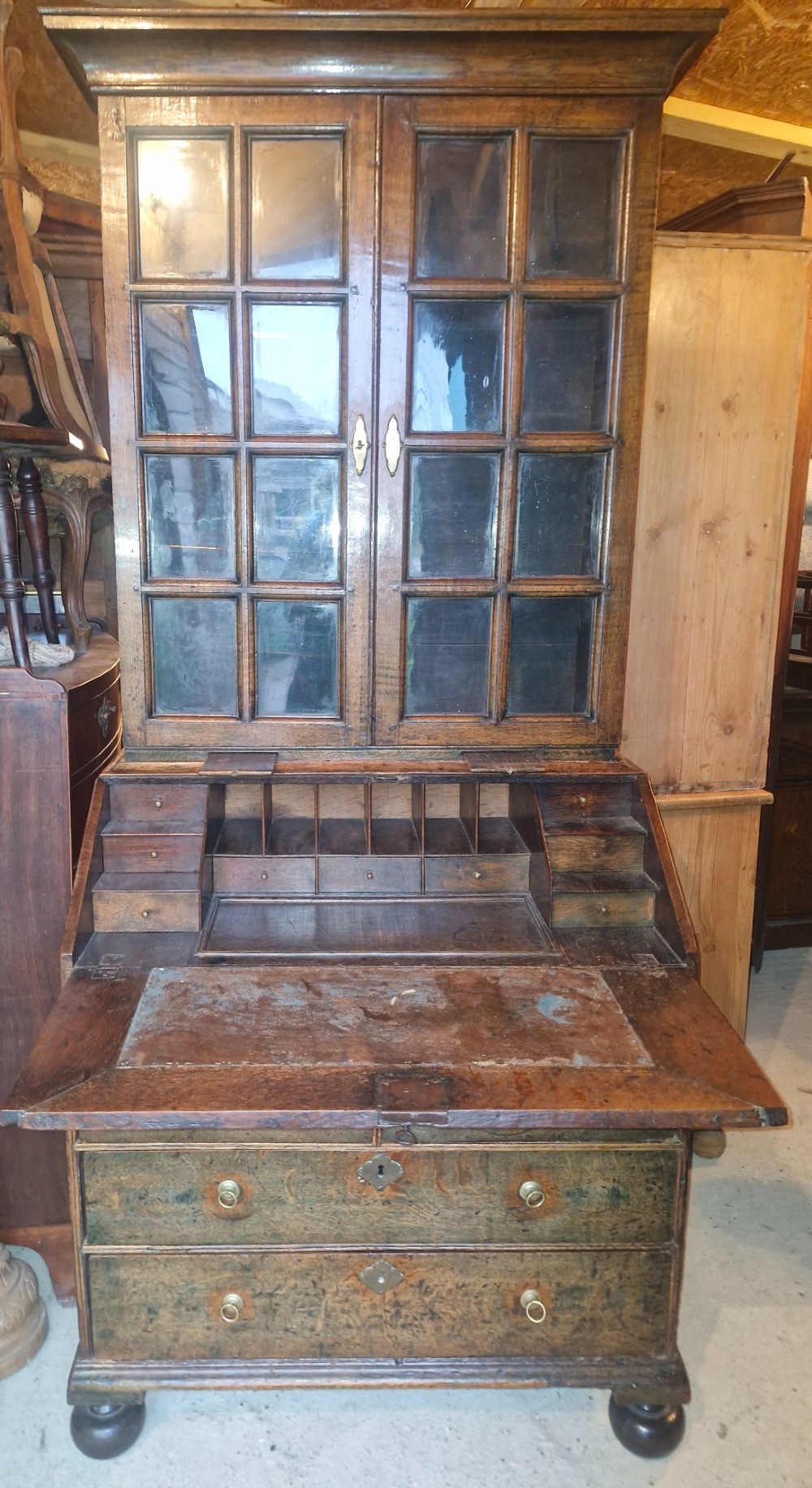 An antique oak bureau bookcase featuring a two-door glazed upper section, a slant-front writing desk, candle slides, and lower drawers raised on bun feet. View IV