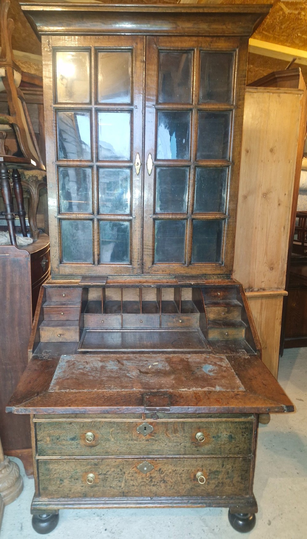 An antique oak bureau bookcase featuring a two-door glazed upper section, a slant-front writing desk, candle slides, and lower drawers raised on bun feet. View VII