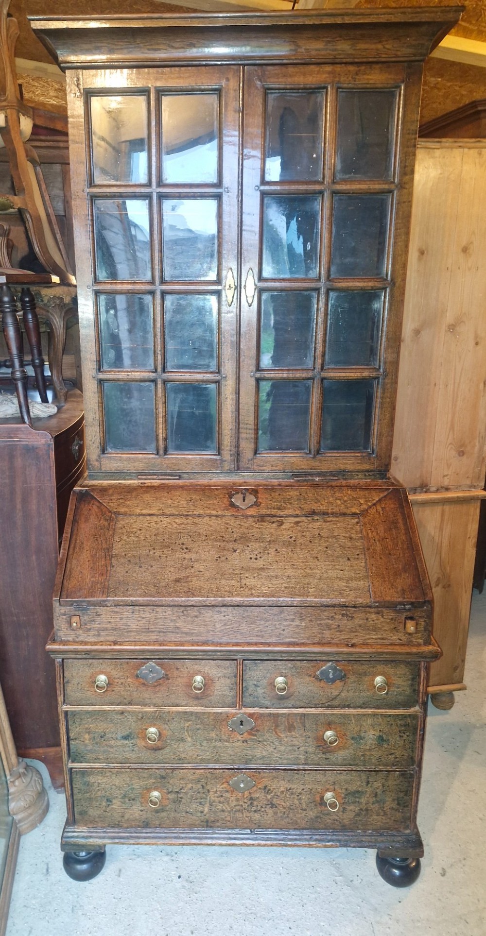 An antique oak bureau bookcase featuring a two-door glazed upper section, a slant-front writing desk, candle slides, and lower drawers raised on bun feet. View XIV