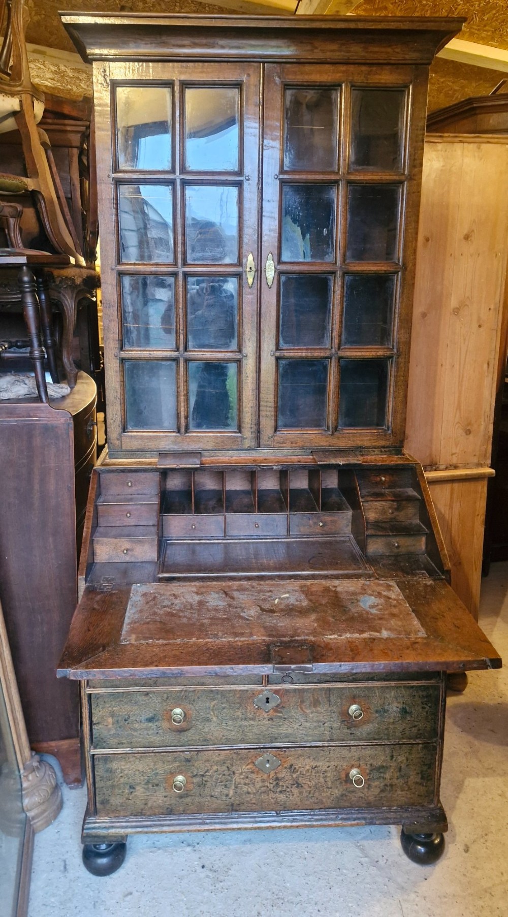 An antique oak bureau bookcase featuring a two-door glazed upper section, a slant-front writing desk, candle slides, and lower drawers raised on bun feet. View XV