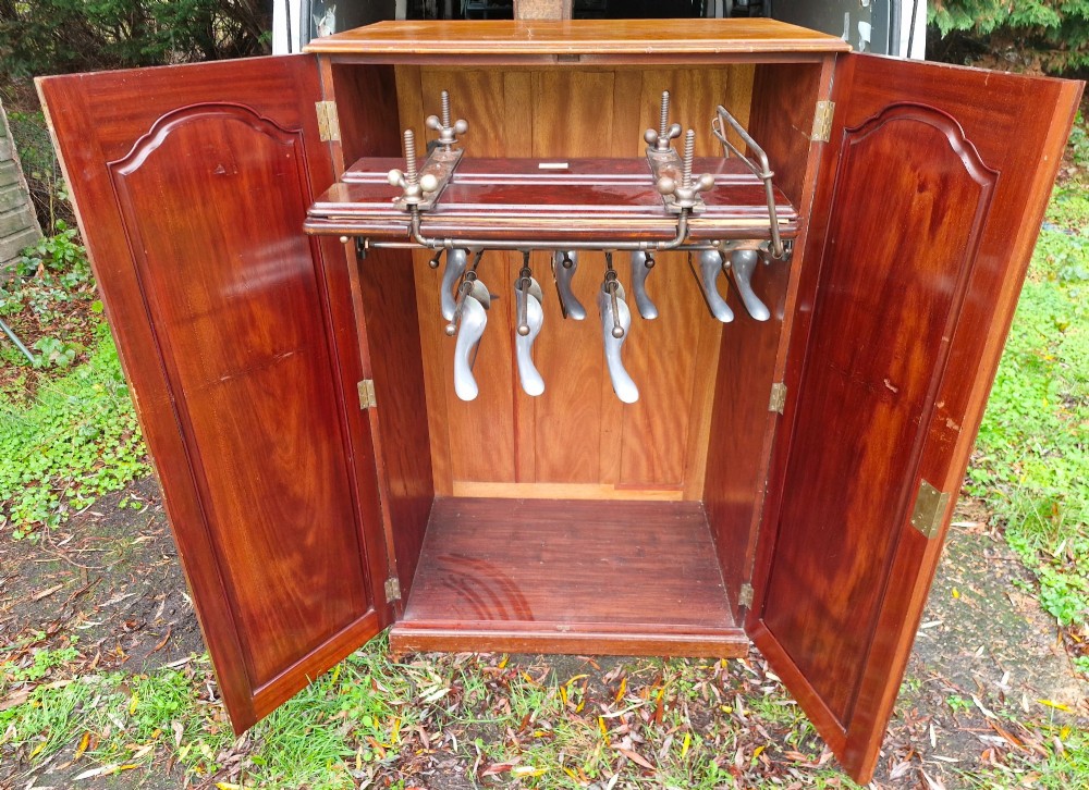 An open twin-door mahogany valet cupboard revealing an internal trouser press mechanism with brass turn-screws and integrated hanging racks.