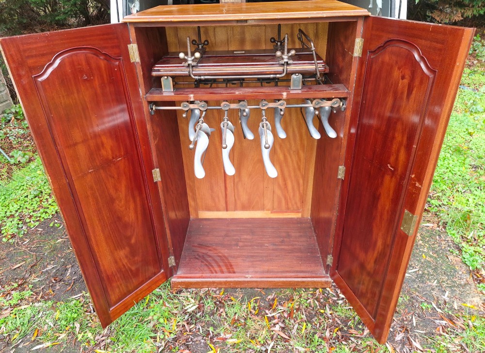An open twin-door mahogany valet cupboard revealing an internal trouser press mechanism with brass turn-screws and integrated hanging racks. View III