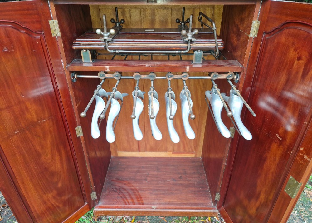 An open twin-door mahogany valet cupboard revealing an internal trouser press mechanism with brass turn-screws and integrated hanging racks. View IX