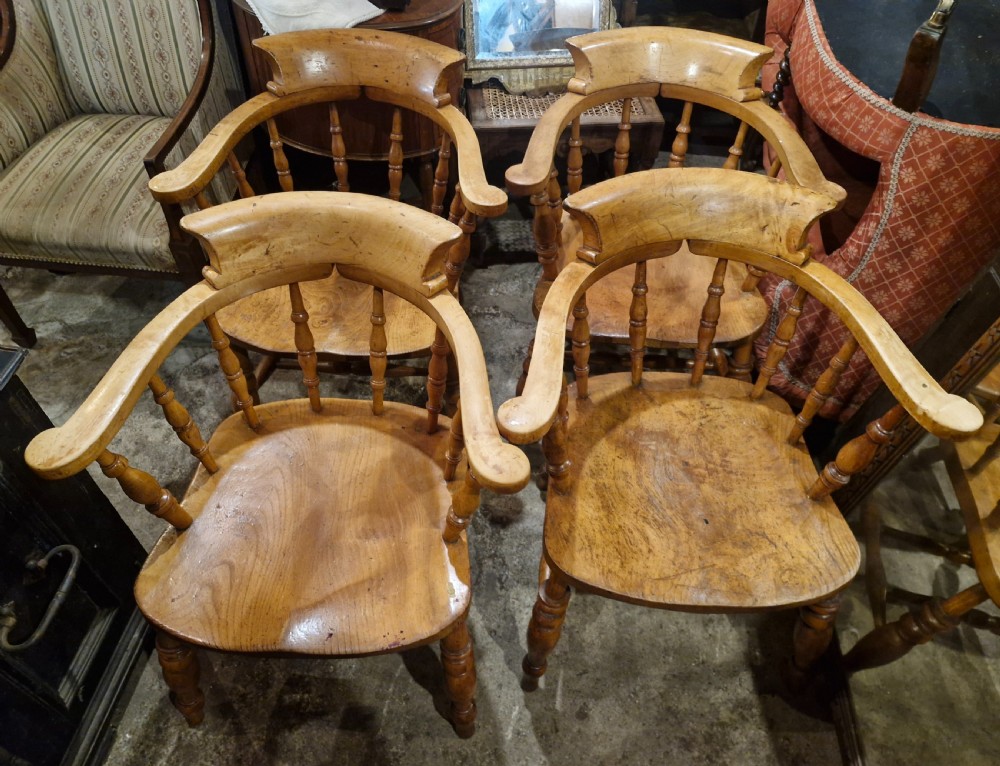 A set of four wooden smokers bow armchairs with continuous curved armrests, turned spindles, shaped seats, and turned legs. View V