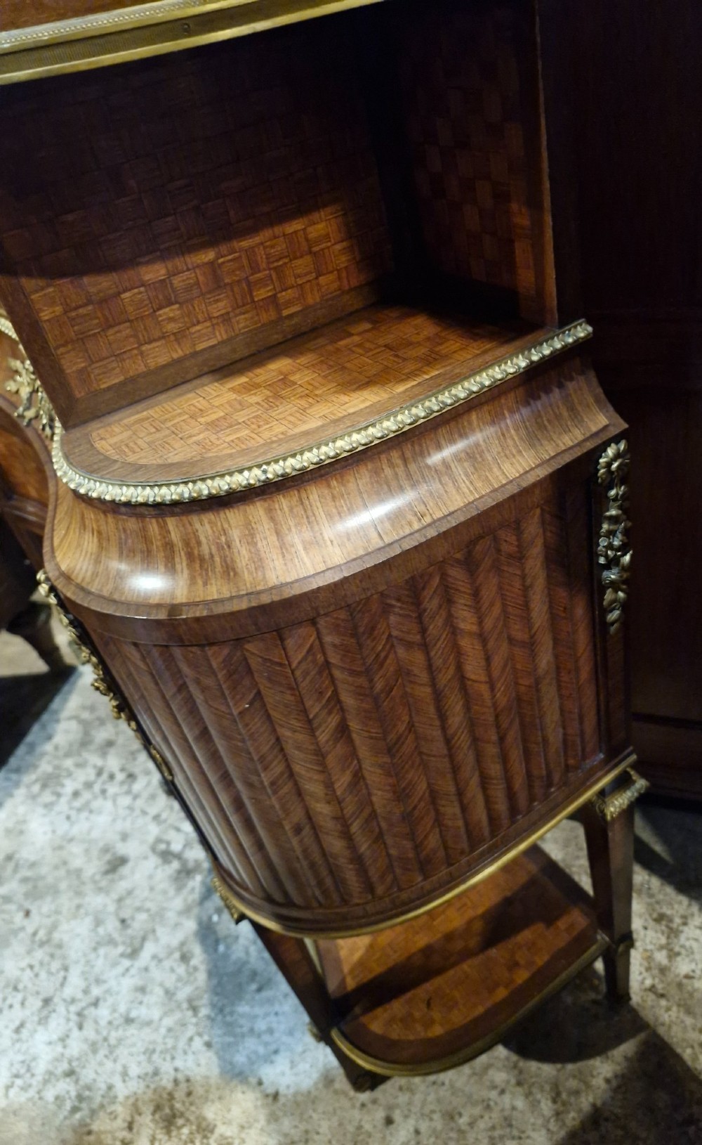 A French Louis XVI style tiered side cabinet crafted with checkerboard parquetry wood veneer, brass gallery, and ornamental ormolu mounts. View V