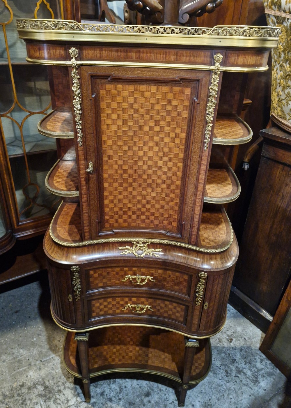 A French Louis XVI style tiered side cabinet crafted with checkerboard parquetry wood veneer, brass gallery, and ornamental ormolu mounts. View VII