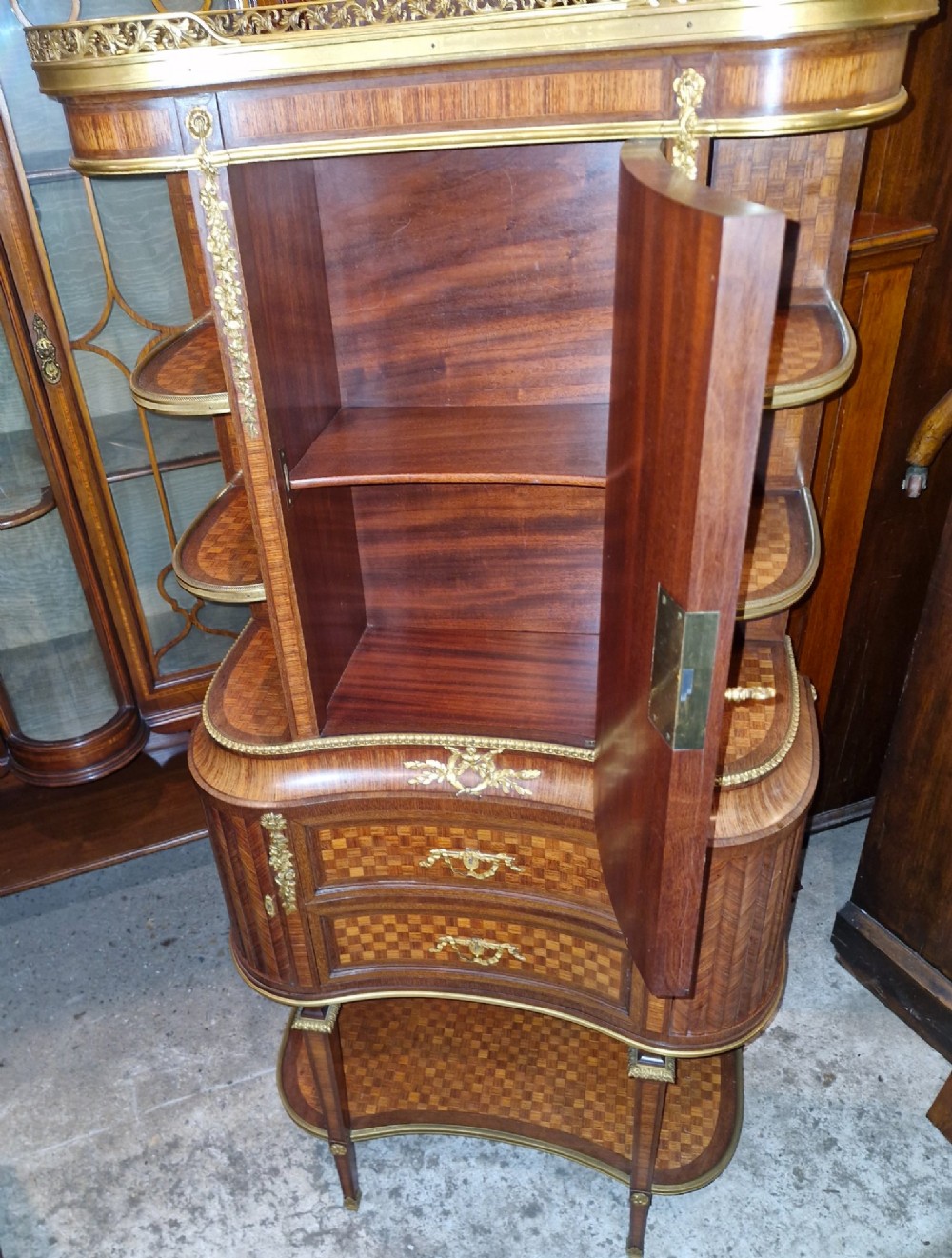 A French Louis XVI style tiered side cabinet crafted with checkerboard parquetry wood veneer, brass gallery, and ornamental ormolu mounts. View X