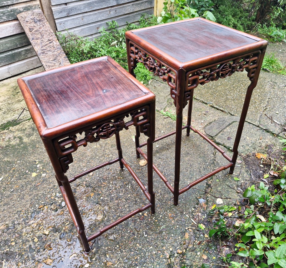 A pair of dark reddish-brown carved Chinese hardwood occasional tables of differing heights featuring bamboo-form legs and carved aprons with fretwork.