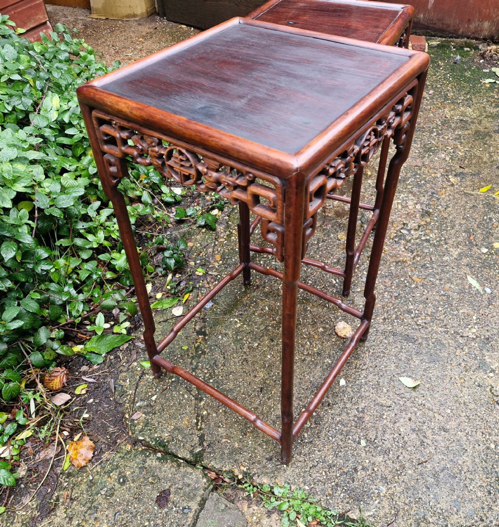 A pair of dark reddish-brown carved Chinese hardwood occasional tables of differing heights featuring bamboo-form legs and carved aprons with fretwork. View V