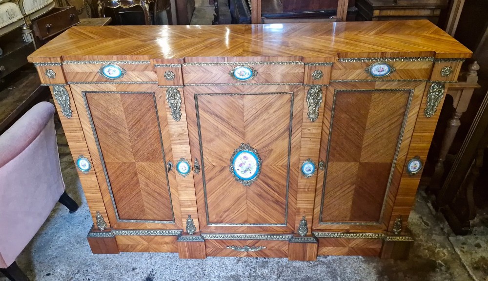 A 19th-century French parquetry side cabinet featuring three doors, brass mounts, and inset porcelain floral plaques.