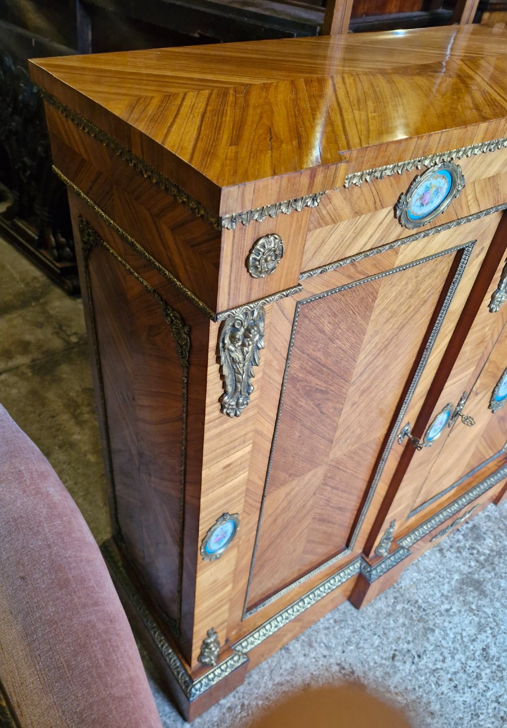 A 19th-century French parquetry side cabinet featuring three doors, brass mounts, and inset porcelain floral plaques. View IV