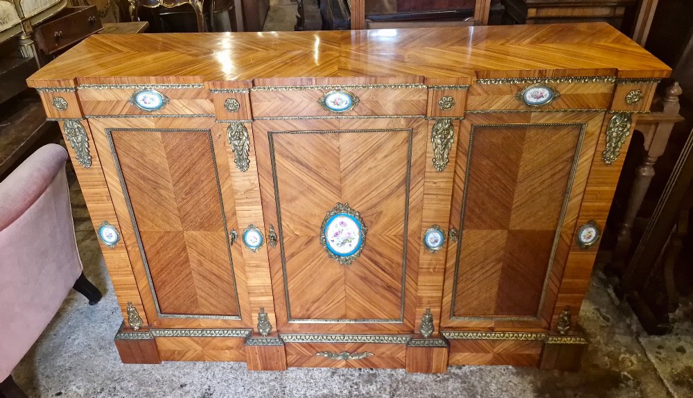 A 19th-century French parquetry side cabinet featuring three doors, brass mounts, and inset porcelain floral plaques. View IX
