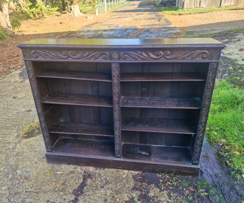 A low late Victorian open-front dark oak bookcase with two compartments, adjustable shelving, carved scrolling frieze, and detailed pilasters.