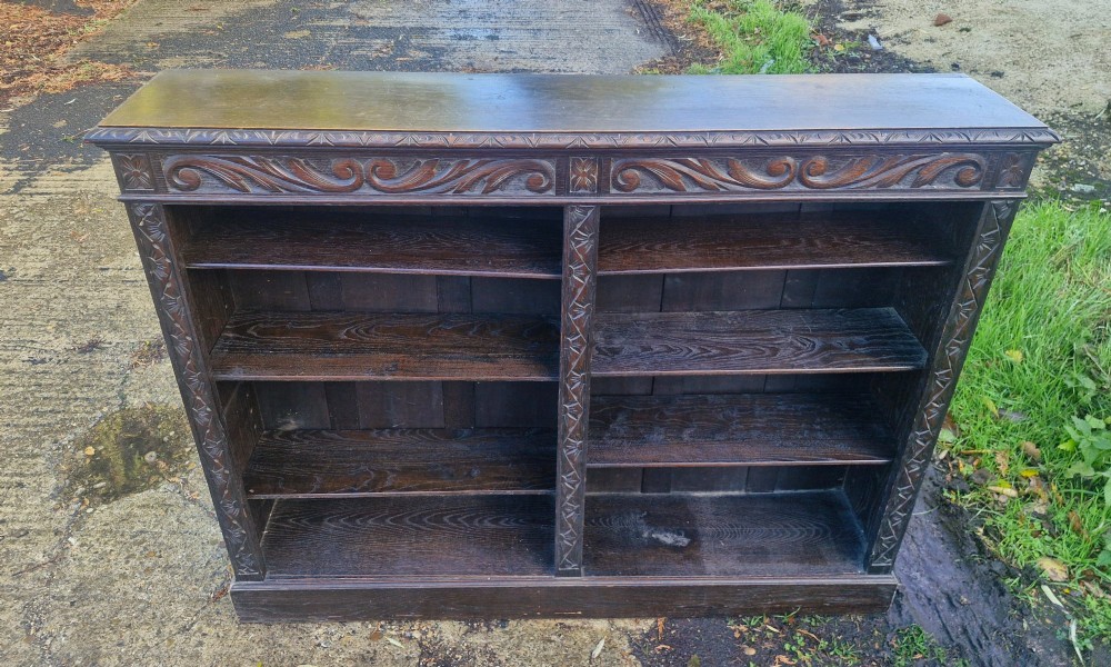 A low late Victorian open-front dark oak bookcase with two compartments, adjustable shelving, carved scrolling frieze, and detailed pilasters. View II