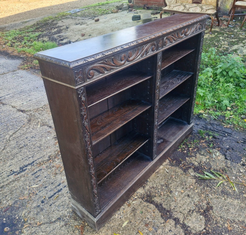 A low late Victorian open-front dark oak bookcase with two compartments, adjustable shelving, carved scrolling frieze, and detailed pilasters. View IV