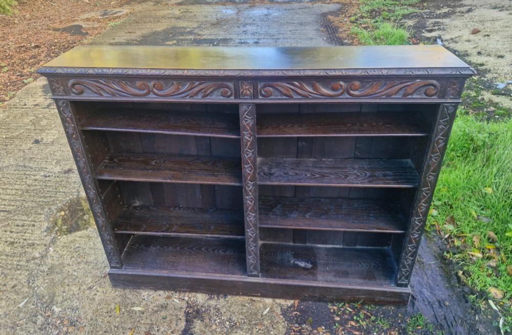 A low late Victorian open-front dark oak bookcase with two compartments, adjustable shelving, carved scrolling frieze, and detailed pilasters. View V