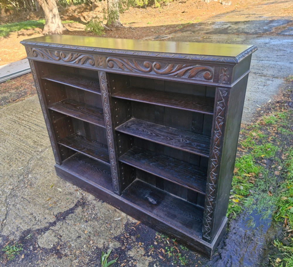 A low late Victorian open-front dark oak bookcase with two compartments, adjustable shelving, carved scrolling frieze, and detailed pilasters. View VI