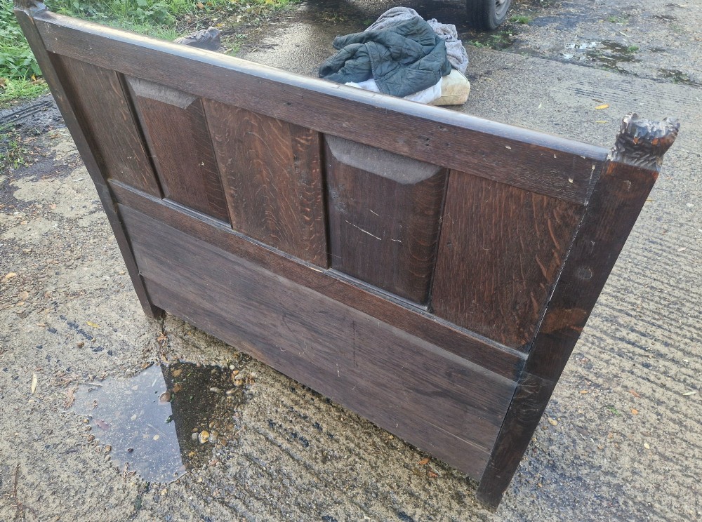 A dark carved oak hall bench featuring a raised back with carved figural and botanical panels, carved armrests, and a hinged storage box base. View II