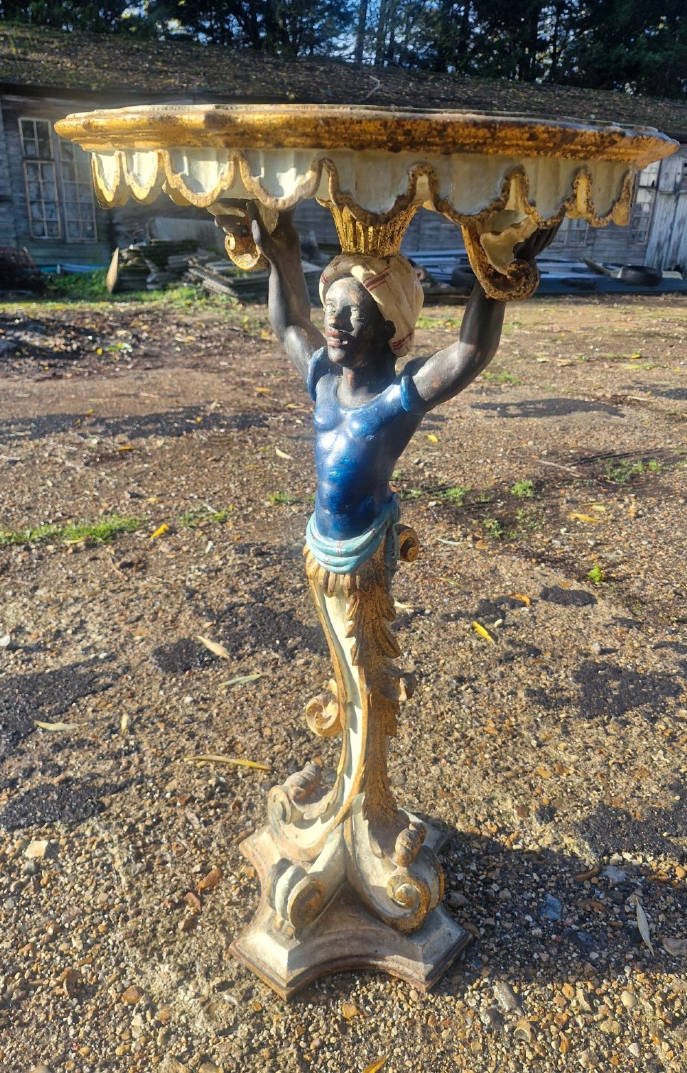 A carved and polychrome painted Italian Blackamoor pedestal stand featuring a figure in a blue top supporting a circular scalloped table top over a gilded scroll base. View III