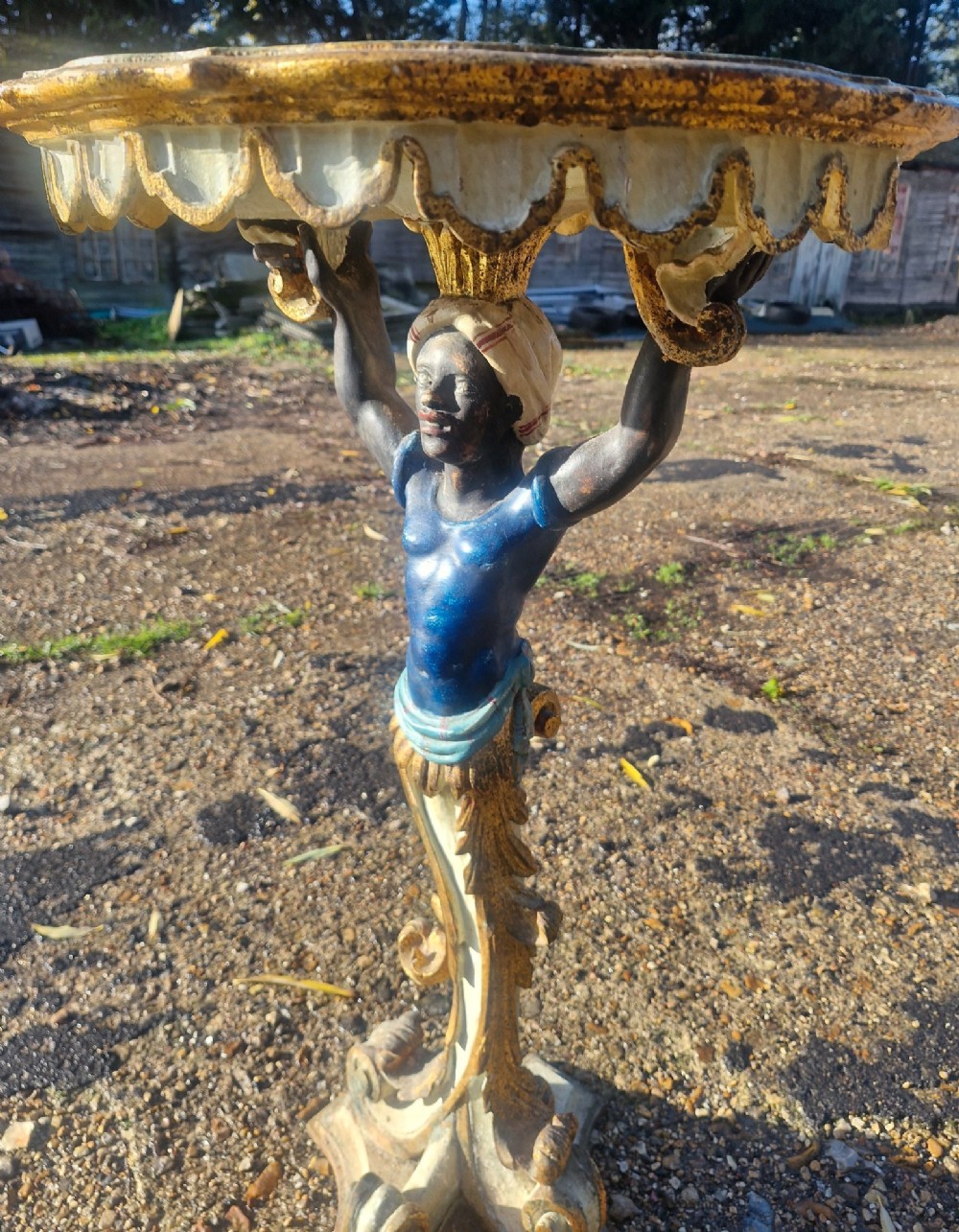 A carved and polychrome painted Italian Blackamoor pedestal stand featuring a figure in a blue top supporting a circular scalloped table top over a gilded scroll base. View IV
