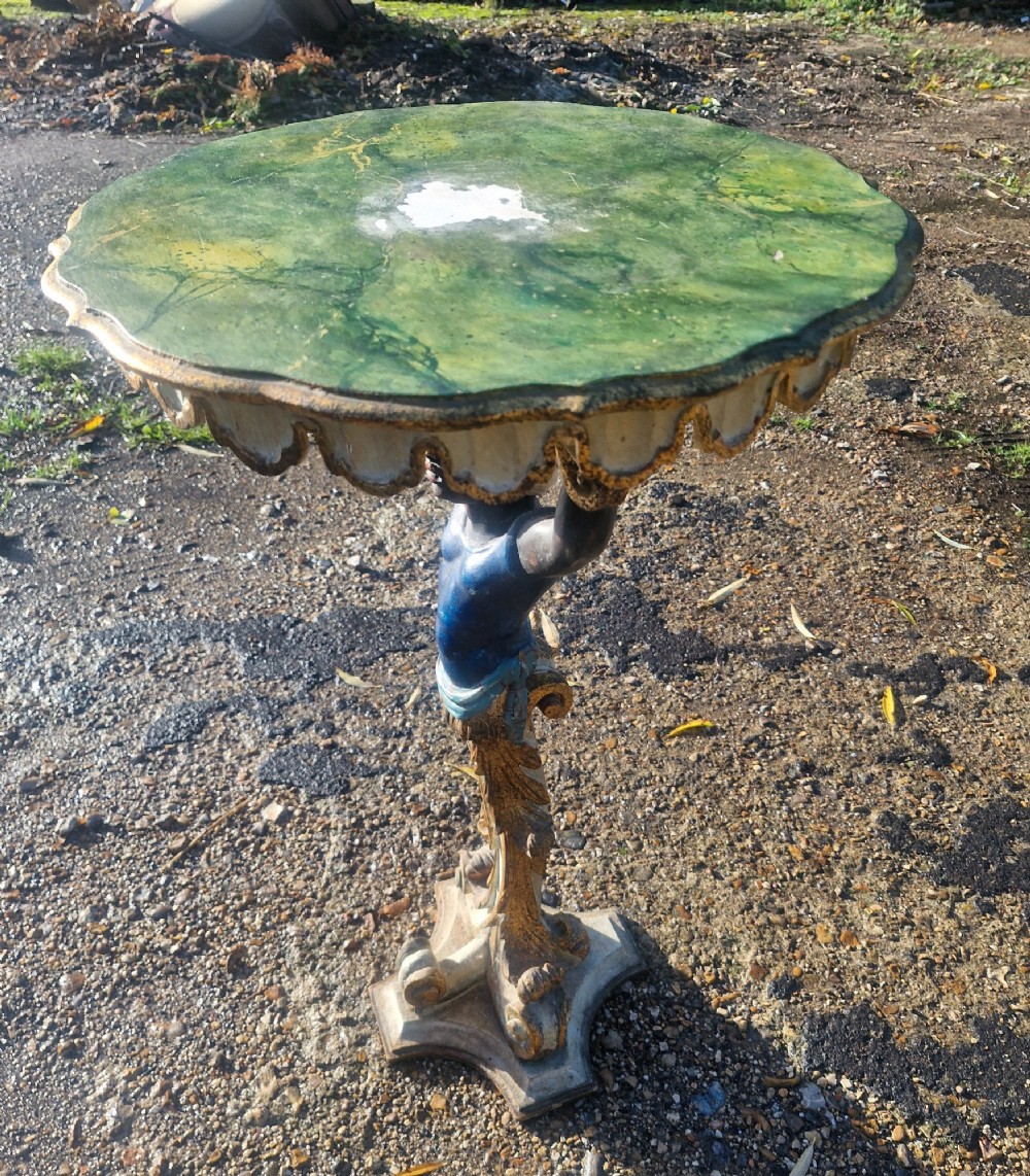 A carved and polychrome painted Italian Blackamoor pedestal stand featuring a figure in a blue top supporting a circular scalloped table top over a gilded scroll base. View VII