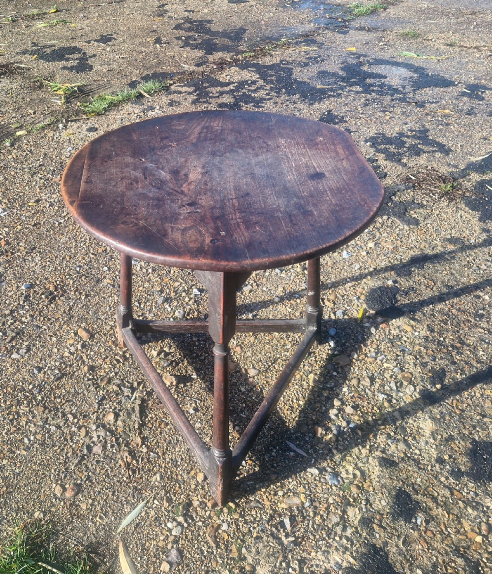 An early 19th-century dark oak cricket table featuring a circular top supported by three turned legs and a lower triangular stretcher.