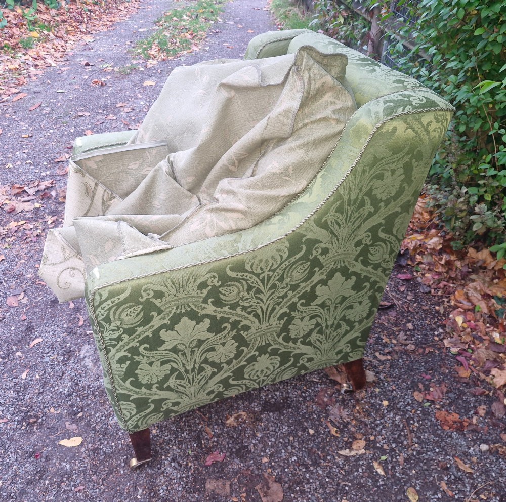 An Edwardian armchair upholstered in patterned green damask fabric with matching braided trim, supported on square tapered mahogany legs with brass castors. View V