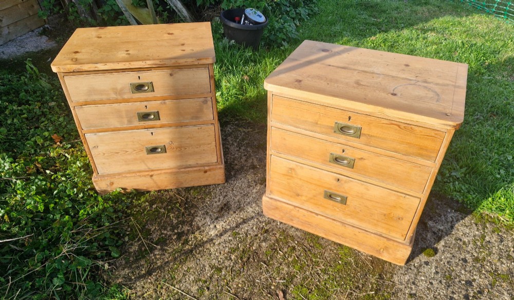 A pair of three-drawer pine bedside chests featuring recessed brass handles and plinth bases.